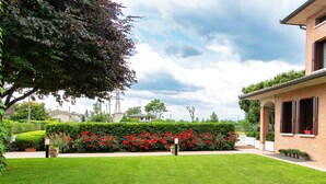 Una propiedad residencial con un césped cuidado, un seto de flores rojas y una casa de ladrillo con balcón.