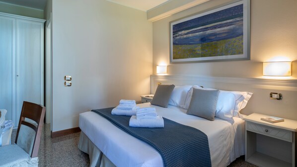 A hotel room with a neatly made bed, two bedside tables, a chair, and a painting on the wall. - Borgo Tabari Mondrian (Mussolente)