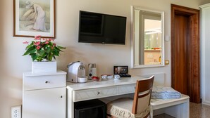 Habitación de hotel con un escritorio blanco, un televisor montado en la pared, un espejo y una puerta que da al baño.
