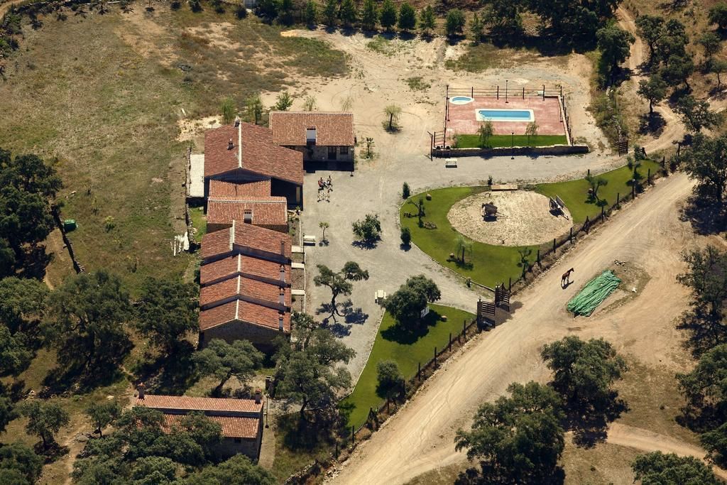 Vista aérea de uma propriedade com um edifício grande, piscina e área ajardinada.