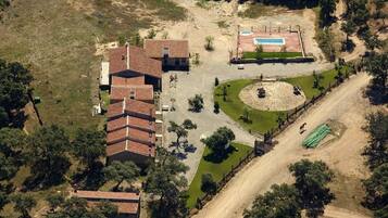 Vista aérea de uma propriedade com um edifício grande, piscina e área ajardinada.