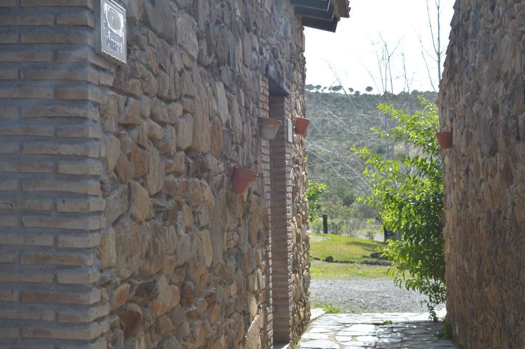 A stone building with a brick section, a pathway leading to a green area, and a sign on the wall.