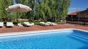 Piscina con sillas reclinables blancas y una sombrilla 'Cruzcampo'.