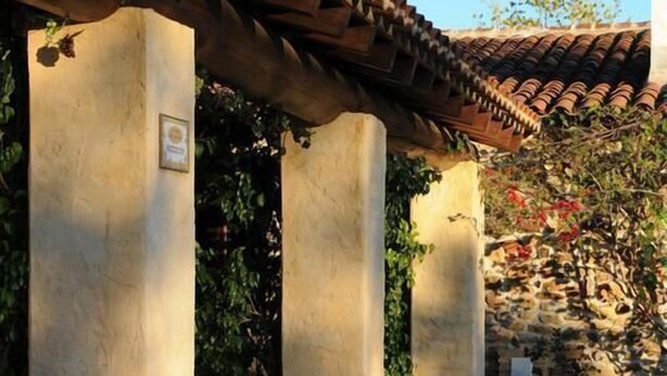 Un patio con techo de tejas, columnas de piedra, plantas en macetas y mobiliario exterior.