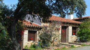 Un edificio rústico de piedra con techo de tejas, puerta de madera y una pequeña zona de estar al aire libre con sillas de metal.