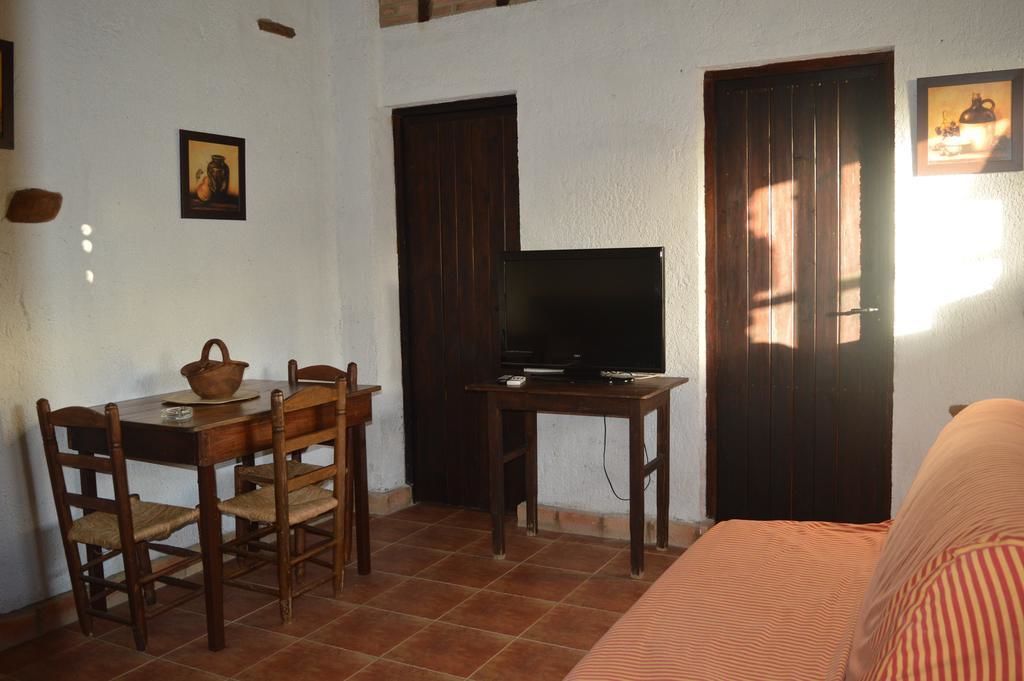 A room with a bed, a TV on a wooden table, a dining table with chairs, and a door.