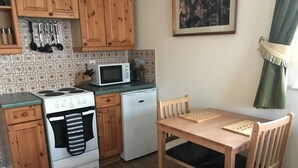 A compact kitchen with wooden cabinets, a stove, a microwave, and a small refrigerator. - One bedroom holiday home near the Snowdonia National Park (Caernarfon)