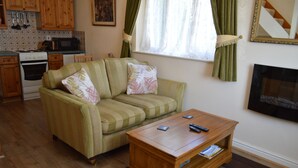 A living room with a striped sofa, a wooden coffee table, a television, and a kitchen area with wooden cabinets and a microwave. - One bedroom holiday home near the Snowdonia National Park (Caernarfon)