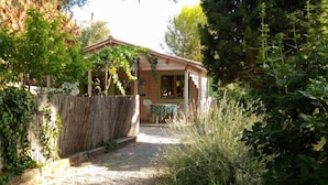 Een houten huis met een overdekte veranda, omgeven door weelderige begroeiing en een bamboombordeling.