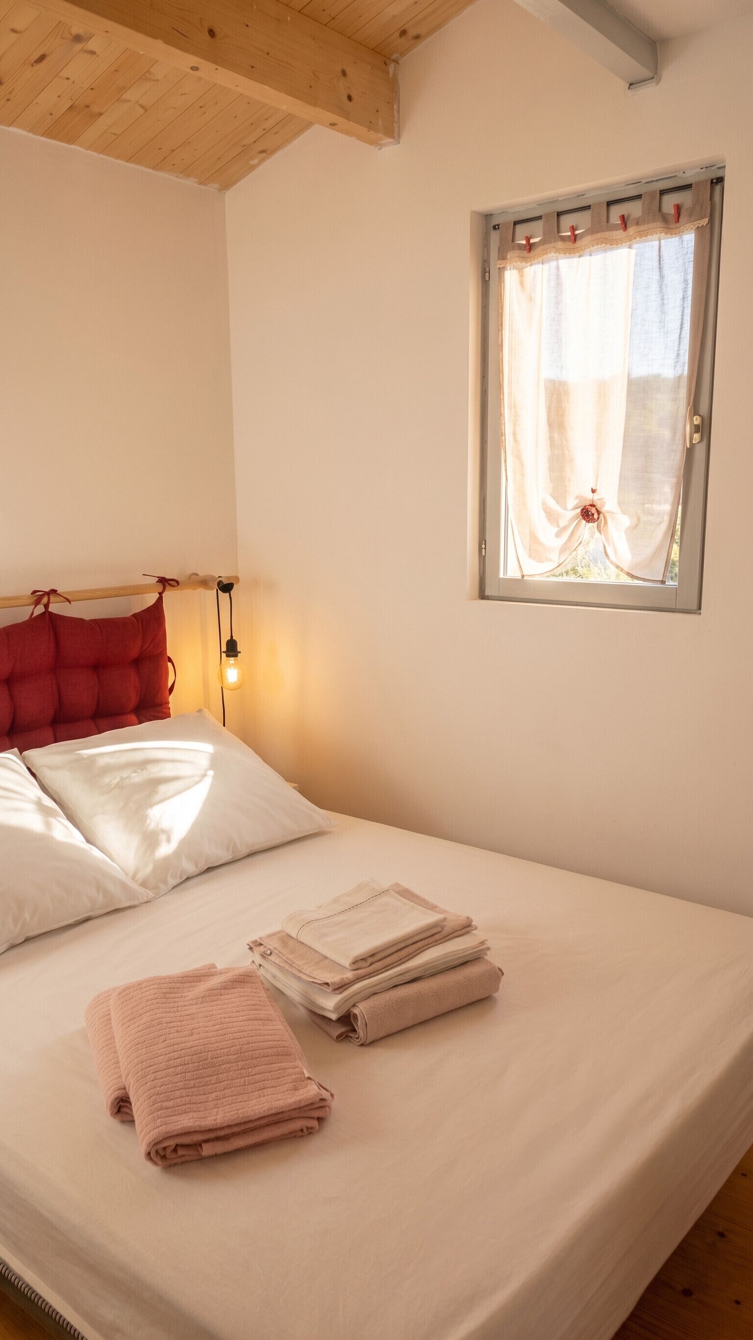 A bed with pillows, a window with curtains, a bedside lamp, and folded towels.