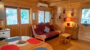 Een houten chalet van binnen met een bank, een kleine tafel, een wasmachine en een lamp.
