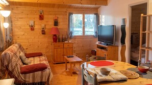 Een gezellig interieur van een chalet met een bank, een eettafel, een televisie en een raam met gordijnen.