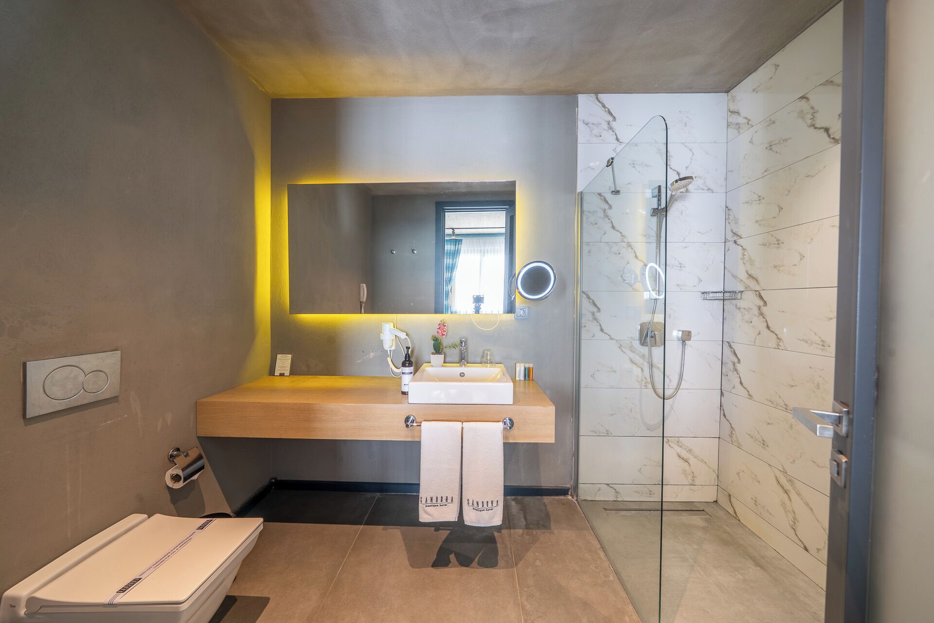 A modern bathroom with a wooden vanity, a glass shower enclosure, and a marble-tiled shower area.