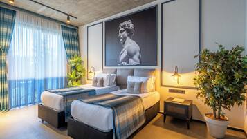 Una habitación de hotel moderna con una cama grande, dos mesitas de noche, una planta en maceta y una obra de arte enmarcada en la pared.