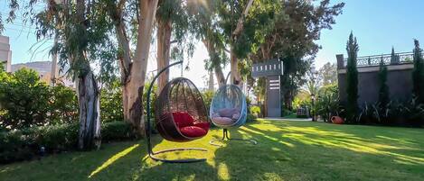 A garden with two hanging chairs, a sign reading "ANDORA," and a well-maintained lawn.