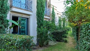 Un estrecho sendero en un jardín, bordeado por abundante vegetación y un edificio con balcón.