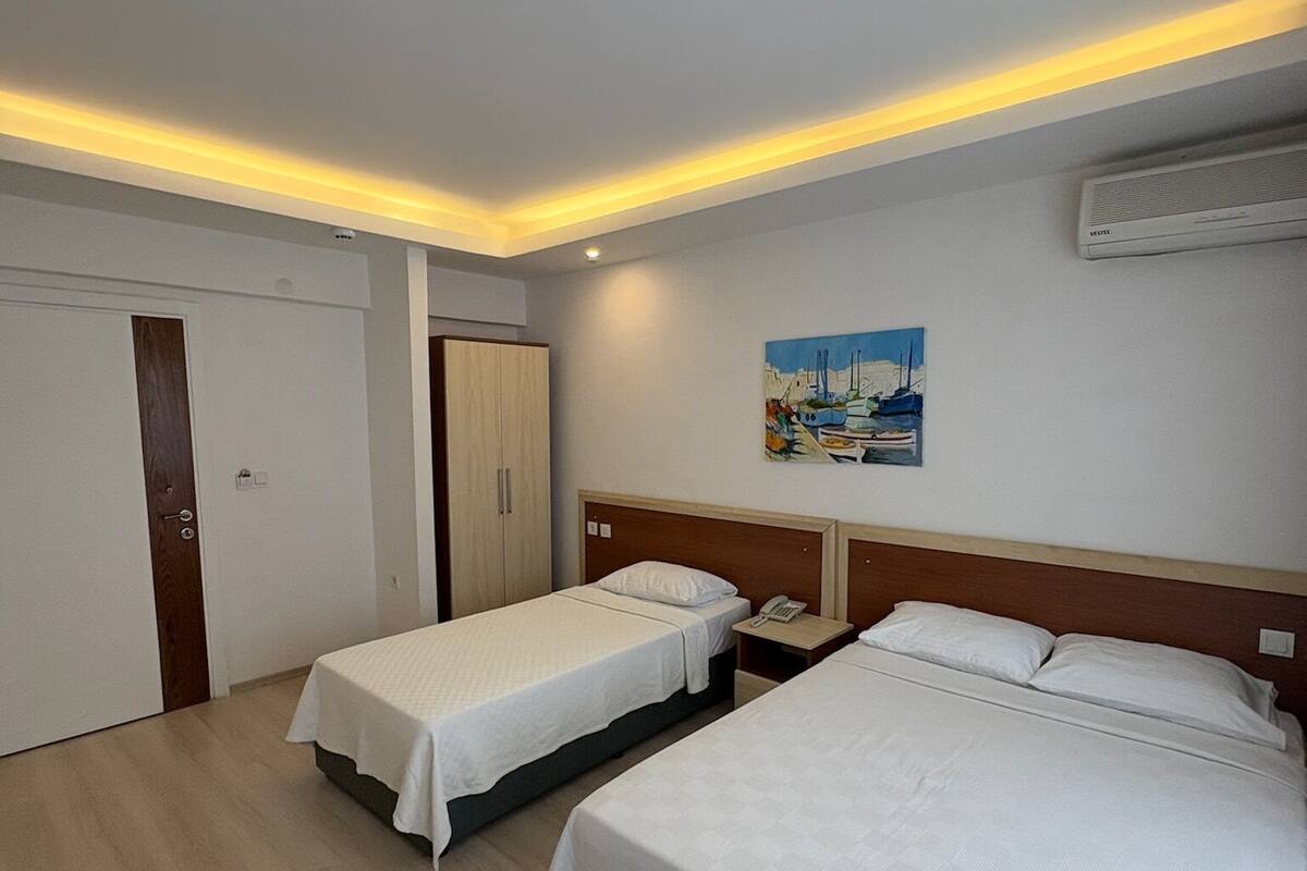 Ein Hotelzimmer mit zwei Einzelbetten, einem Holzschrank, einem Schreibtisch mit Stuhl und einer Wandklimaanlage.