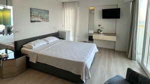 A hotel room with a large bed, bedside table with a phone, a chair, a desk with a mirror, a TV mounted on the wall, and a window with curtains. - Amphora Hotel (Ayvalik)