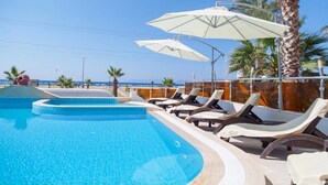 A pool area with lounge chairs and umbrellas, palm trees, and a clear view of the beach. - Amphora Hotel (Ayvalik)