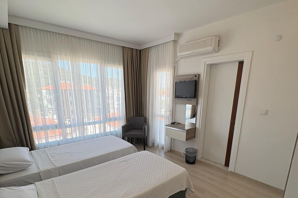 Ein Hotelzimmer mit zwei Betten, einem Schreibtisch, einem Stuhl, einem Fernseher und einem Fenster mit Vorhängen.