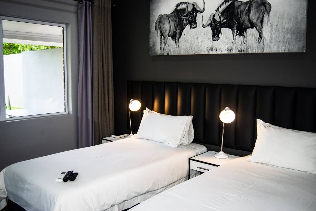 A hotel room with two beds, a large wall painting of wildlife, and a window with curtains.