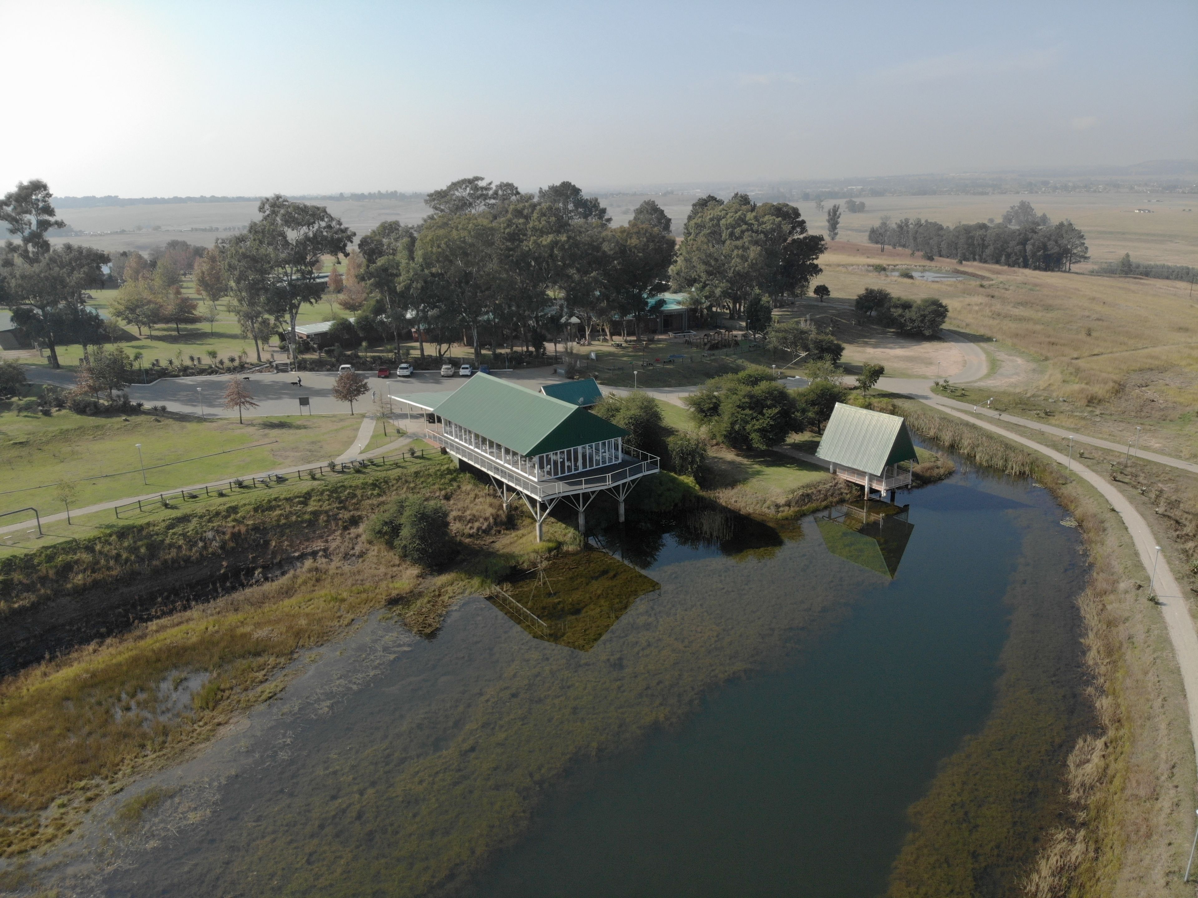 A large building with a green roof, surrounded by a pond and a walking path.