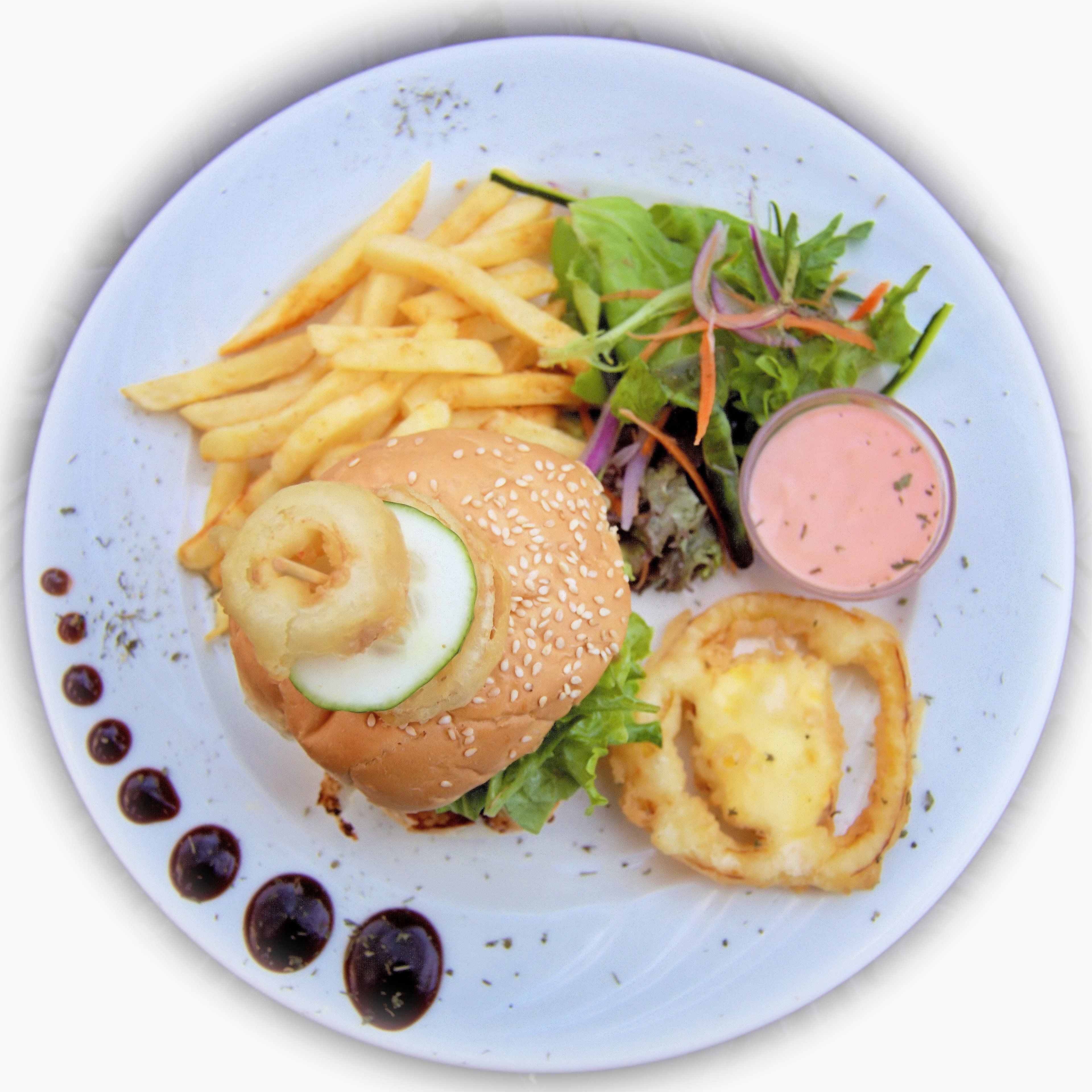 A plate with a burger, fries, salad, and a small container of sauce.