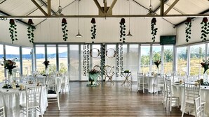 A large hall with wooden flooring and white tables and chairs, decorated with hanging plants and circular wall decorations. - Grey Goose Game Lodge (Newcastle)