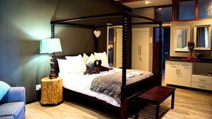 A four-poster bed with a canopy, a bedside lamp, a bench, and a small round table with a lamp. - Grey Goose Game Lodge (Newcastle)