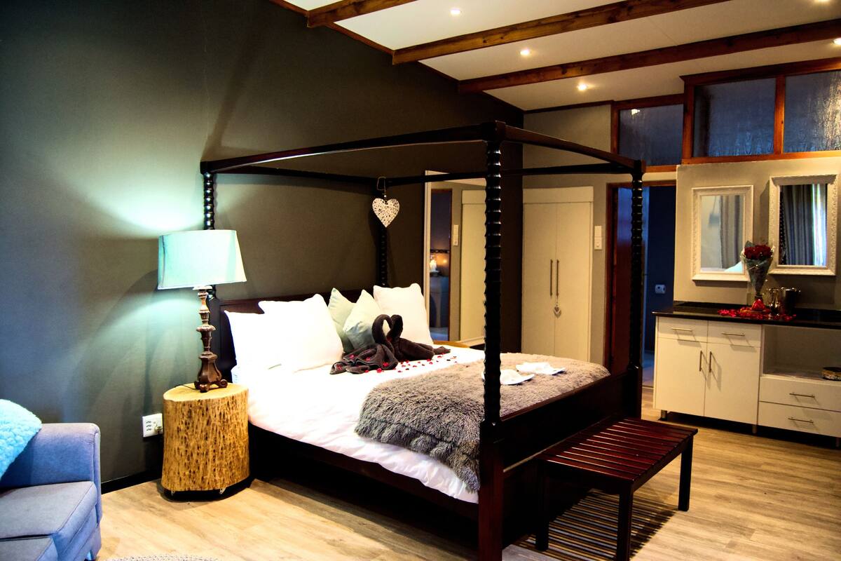 A four-poster bed with a canopy, a bedside lamp, a bench, and a small round table with a lamp.