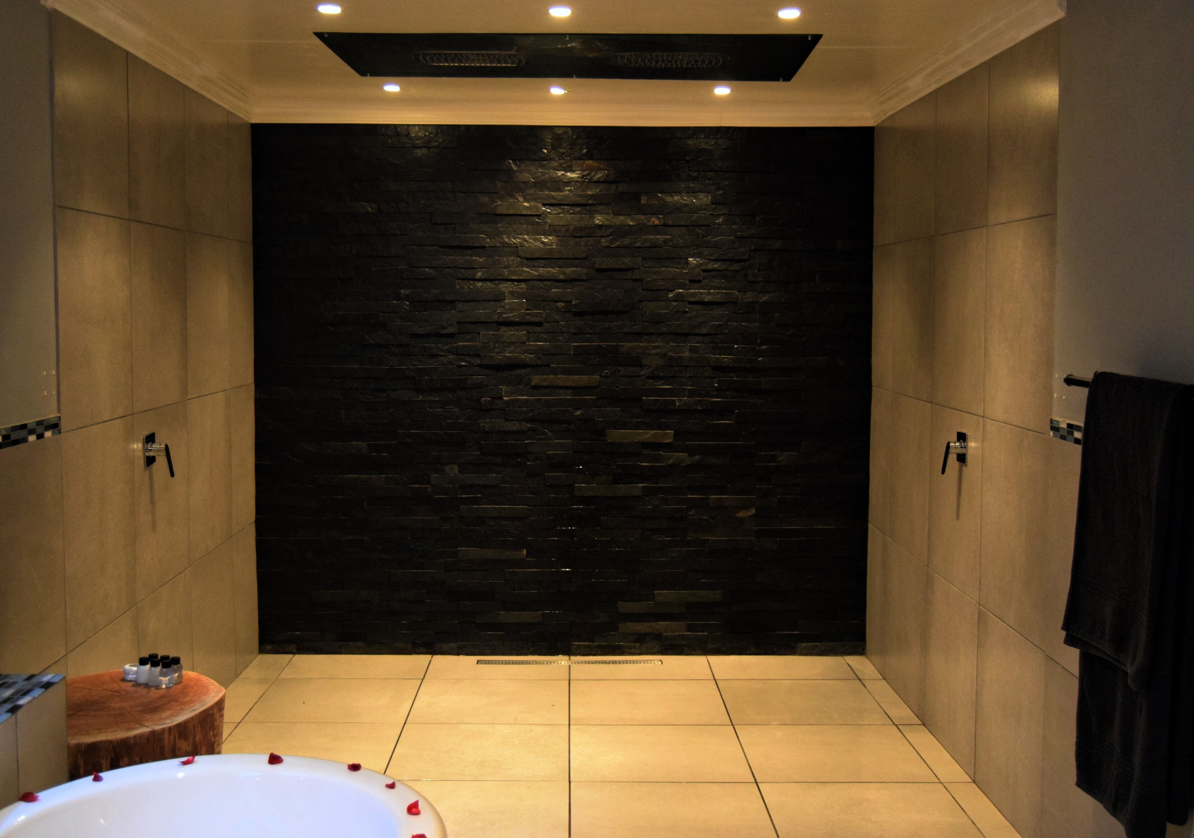 A modern bathroom with a stone wall, a bathtub with rose petals, and a wooden stool.