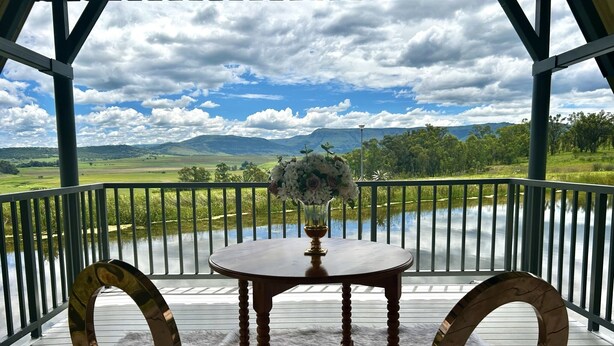 A covered outdoor seating area with a table and chairs, overlooking a lake and distant mountains. - Grey Goose Game Lodge (Newcastle)