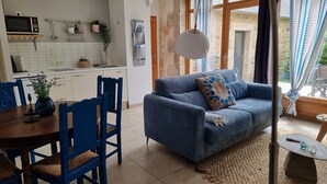 Una sala de estar moderna con un sofá azul, una mesa de comedor con sillas y una cocina al fondo.