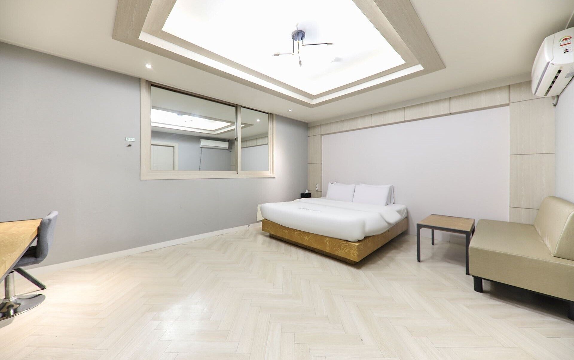 A modern hotel room with a skylight, a large bed, a small table, a sofa, and a mirror.