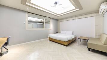A modern hotel room with a skylight, a large bed, a small table, a sofa, and a mirror.