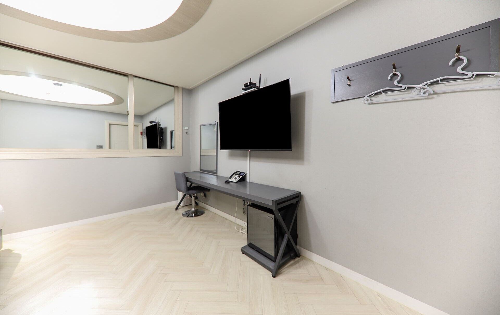 A modern bathroom with a large mirror, a flat-screen TV mounted on the wall, a bench, and a coat rack with hangers.
