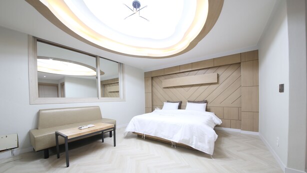 A modern bedroom with a large bed, a bench, a mirror, and a ceiling light fixture. - Eco Hotel (Mokpo)