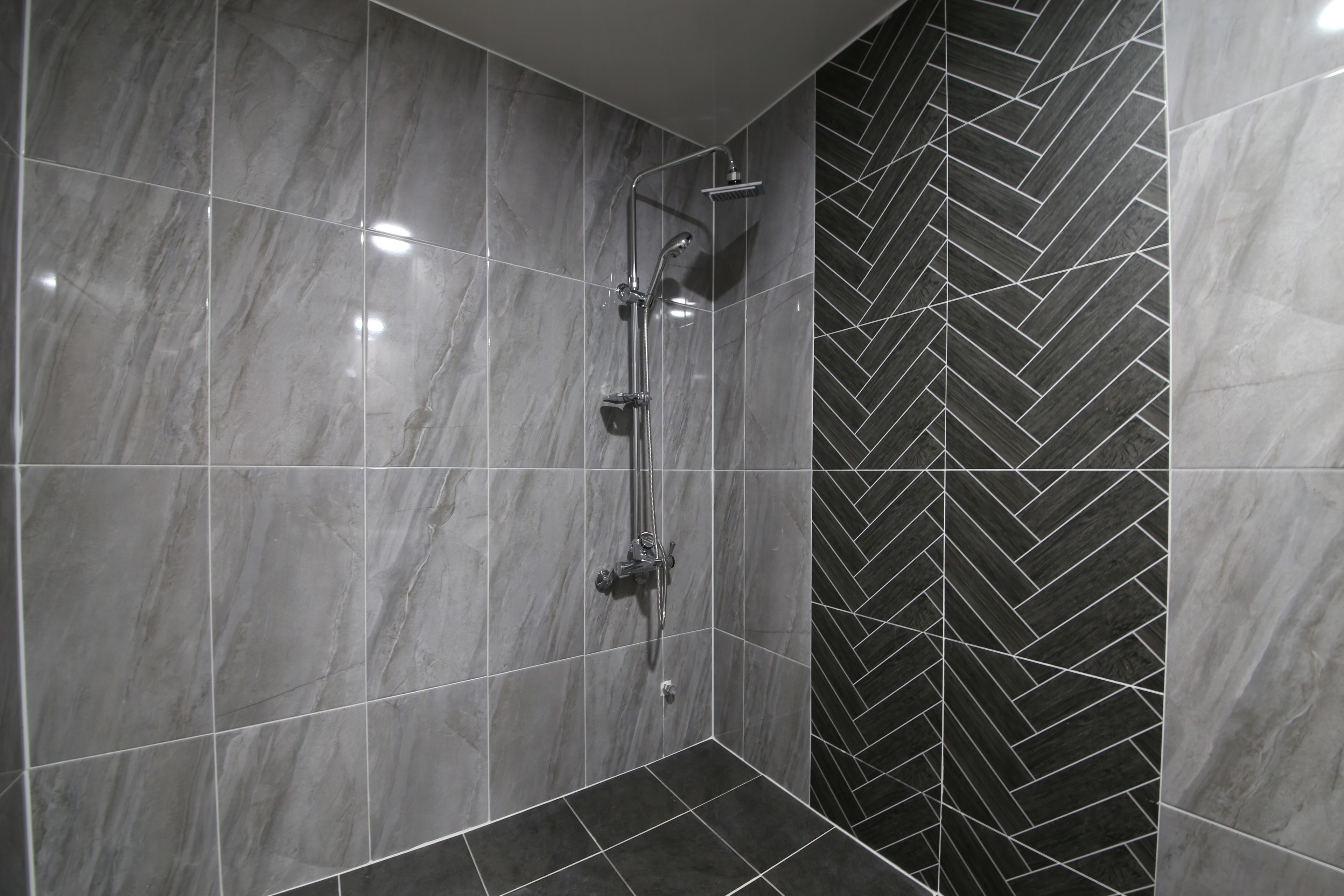 A shower area with a herringbone-patterned wall and a tiled floor.