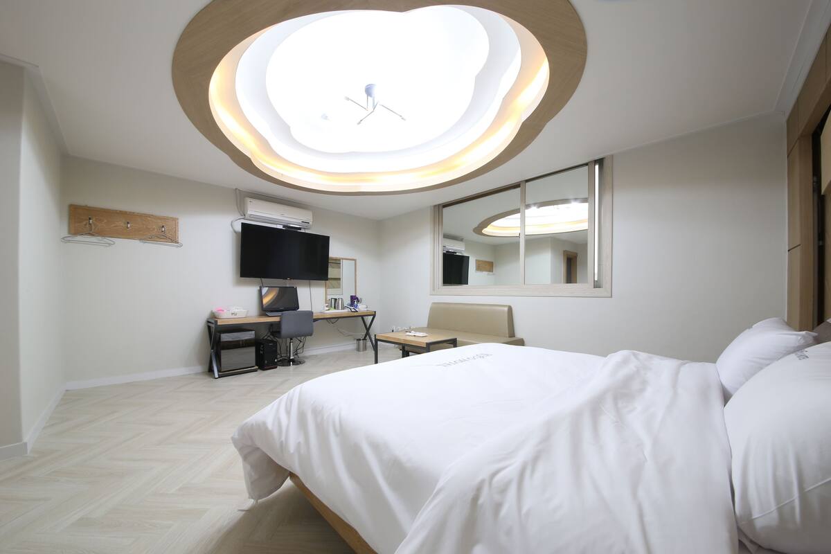 A hotel room with a bed, a desk with a computer, a chair, a TV, and a mirror.