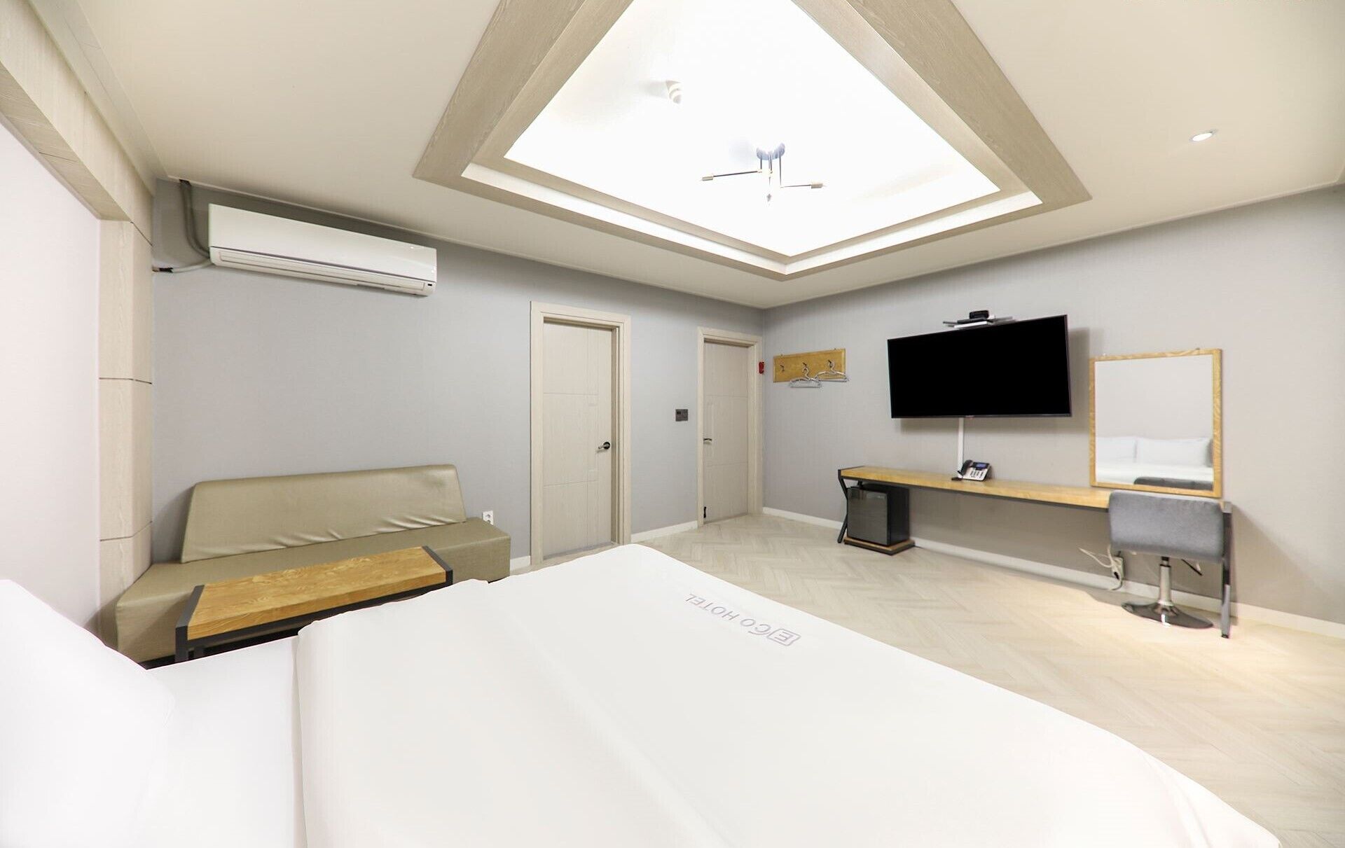 A hotel room with a skylight, a bed, a seating area, a TV, a desk, and a mirror.