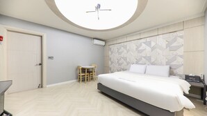 Una habitación de hotel moderna con una cama grande, una pequeña mesa y silla, un tragaluz redondo y un muro con estampado geométrico.