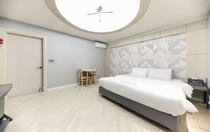 A modern hotel room with a large bed, a small table and chair, a round skylight, and a geometric-patterned wall. - Eco Hotel (Mokpo)