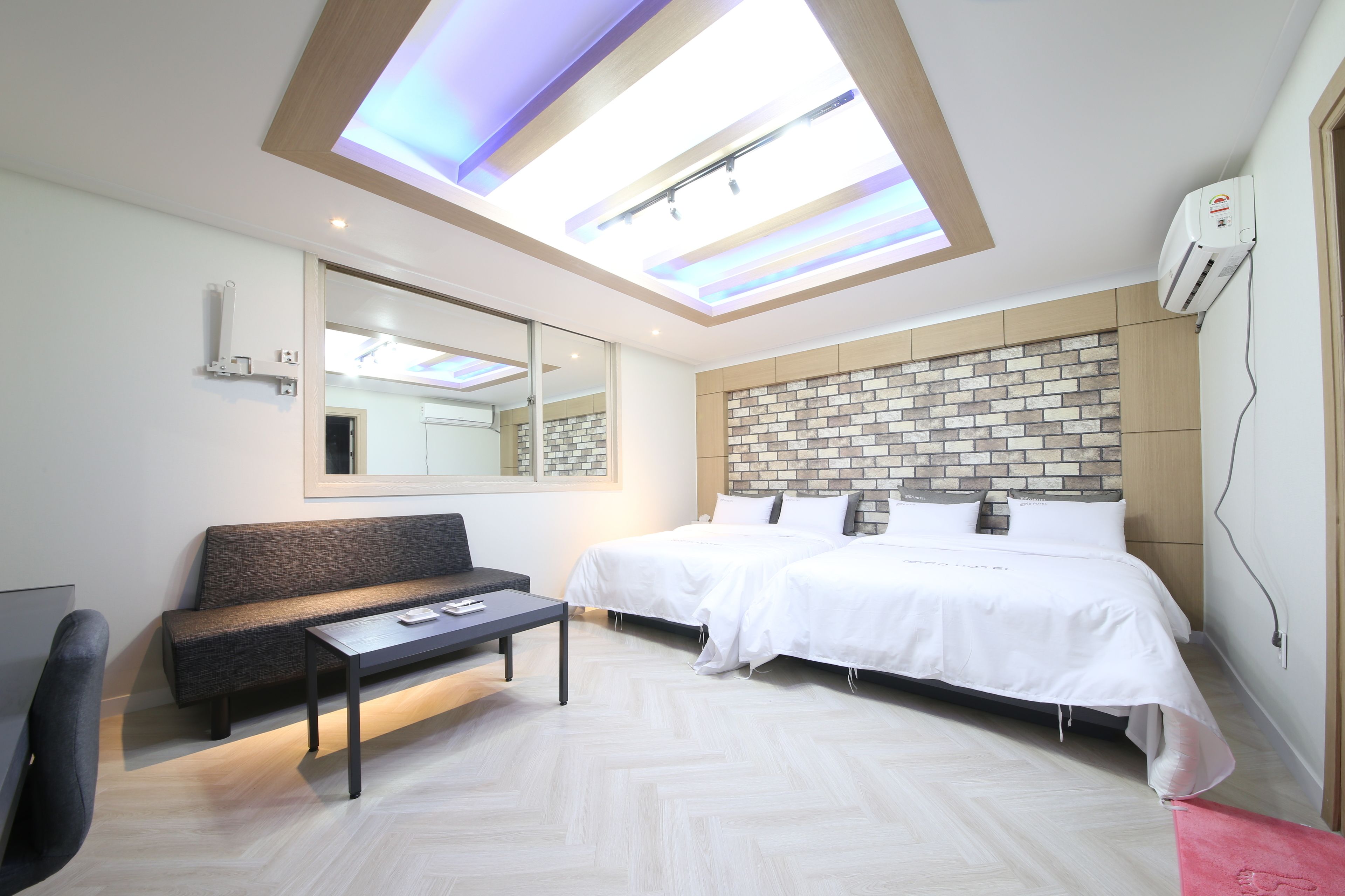 A modern hotel room with a skylight, a large bed, a sofa, a small table, and a mirror.