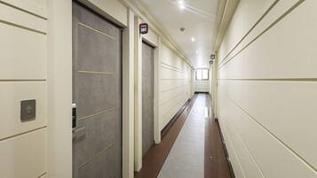 A long, narrow hallway with doors on both sides, a carpeted floor, and a ceiling with recessed lighting.