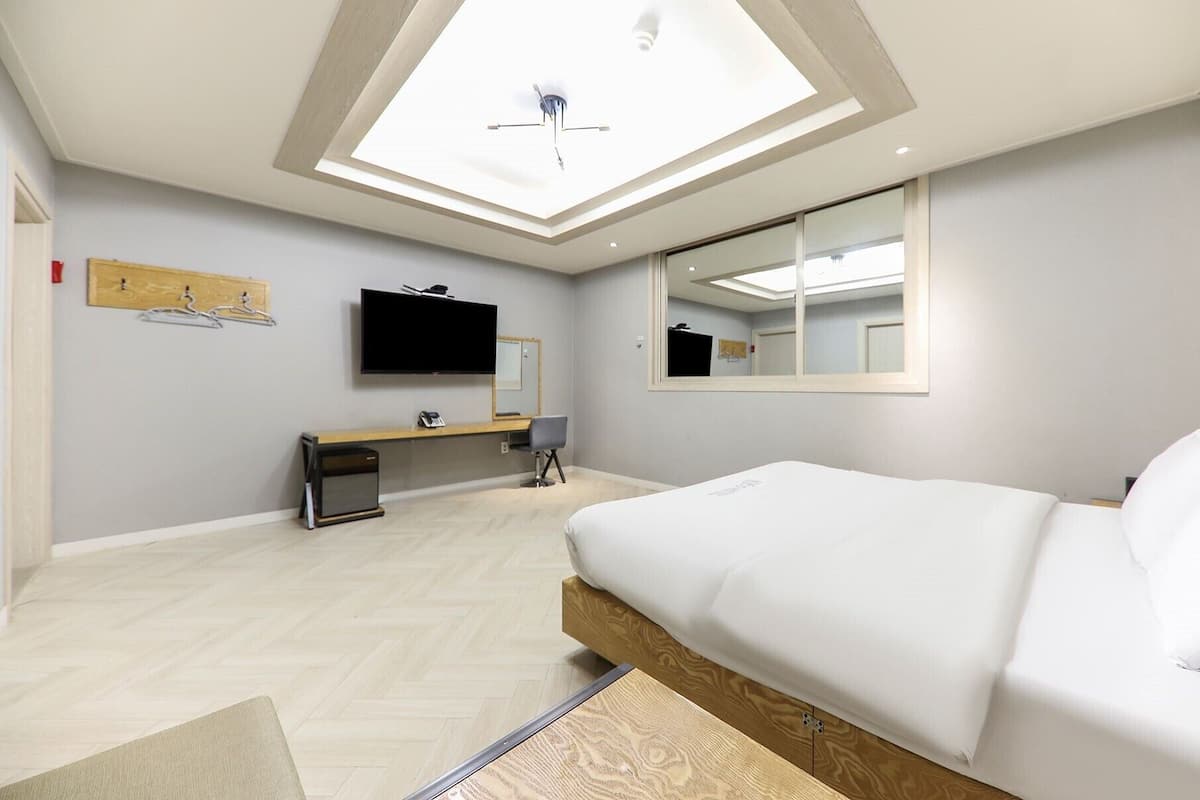 A modern hotel room with a large bed, a flat-screen TV, a desk, and a ceiling skylight.