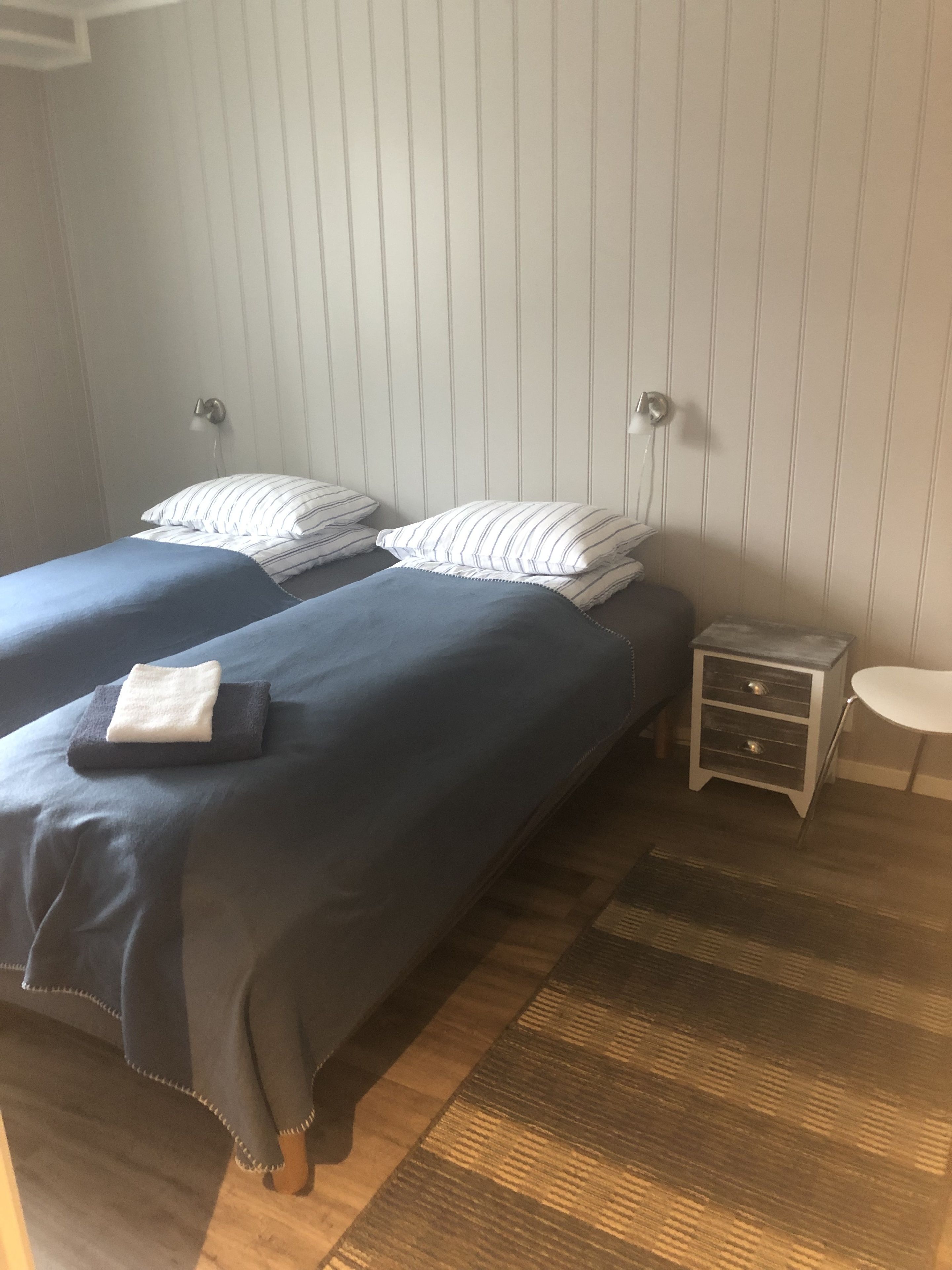 Une chambre avec deux lits, une petite table de chevet et une lampe fixée au mur.