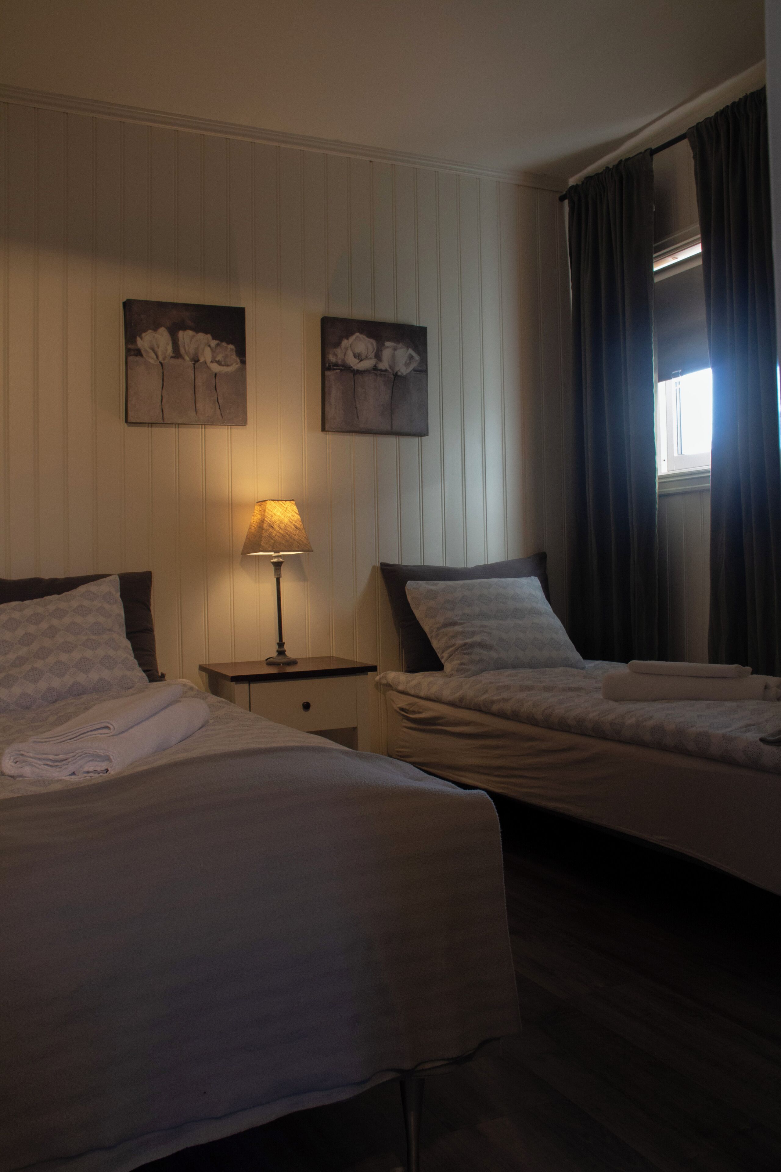 A hotel room with two beds, a nightstand with a lamp, and artwork on the wall.