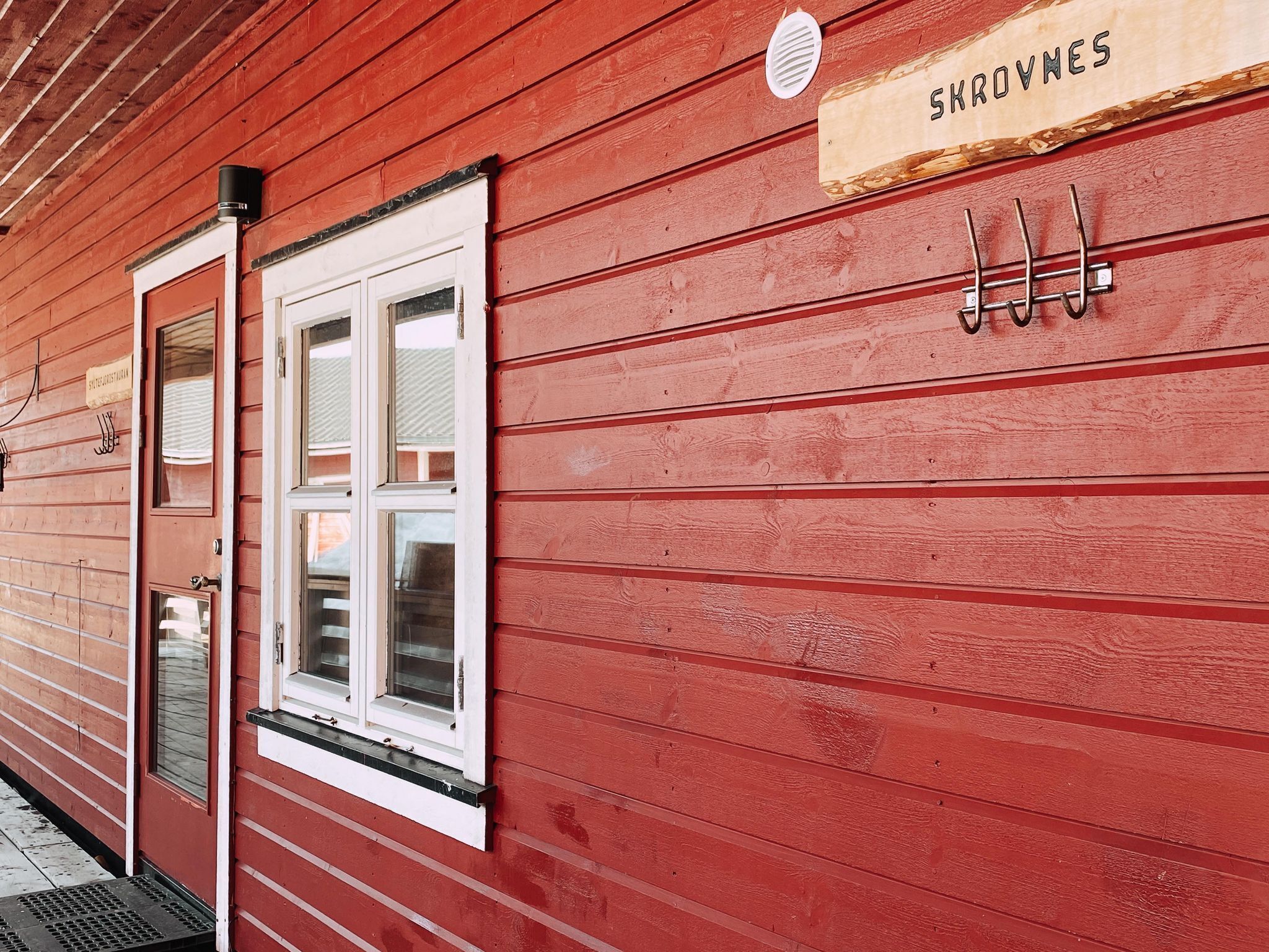 A red wooden building with a white-framed window and a wooden sign above it.