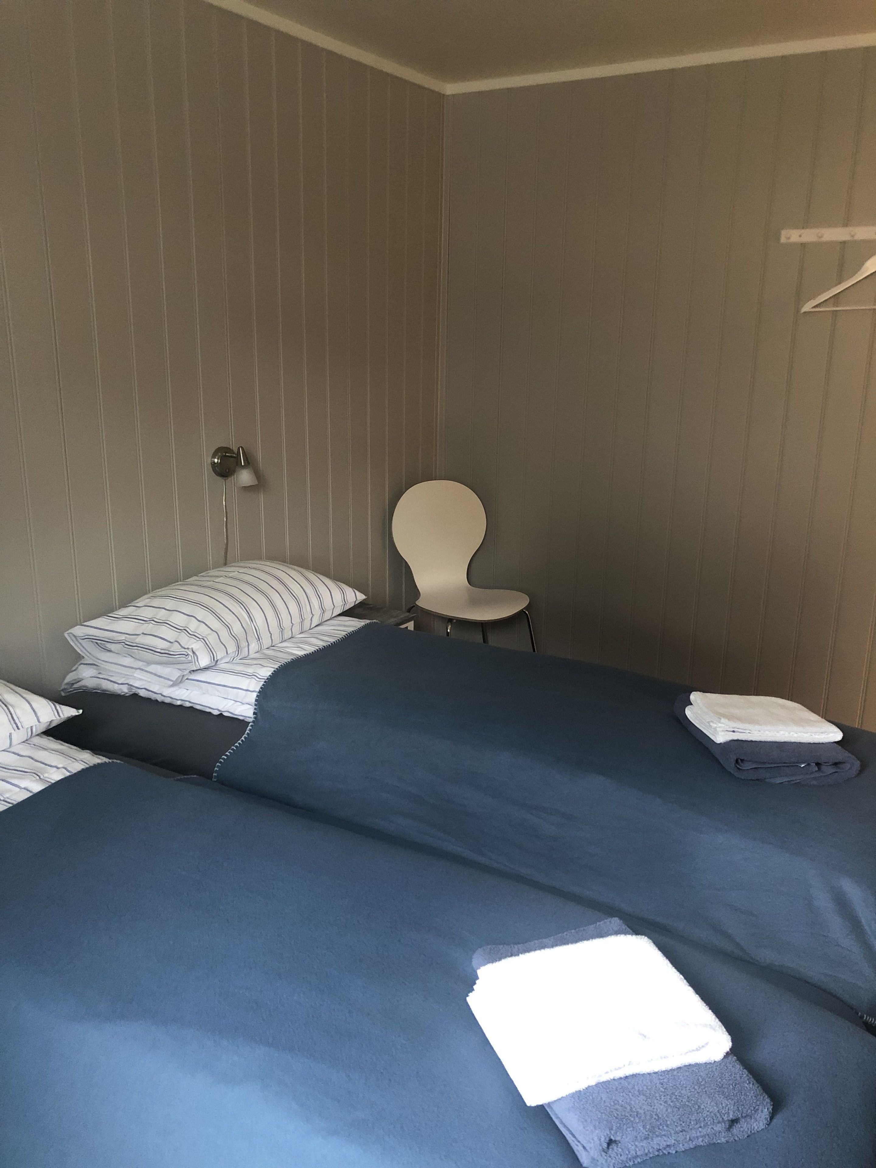 Ein Zimmer mit zwei Betten, einem Sessel und einer Wandlampe.