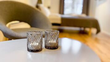 Quarto de hotel moderno com uma cama, uma poltrona cinza e dois vasos de vidro decorativos sobre uma mesa redonda.